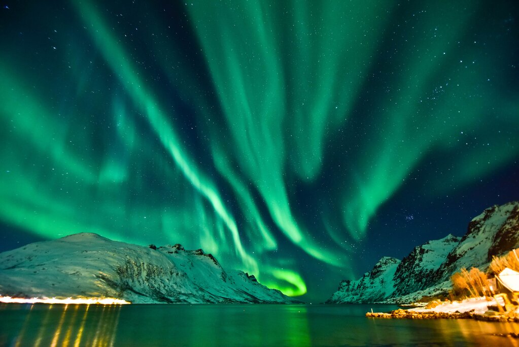 The Aurora Borealis, or Northern Lights, illuminating the sky above a snowy fjord in Norway.